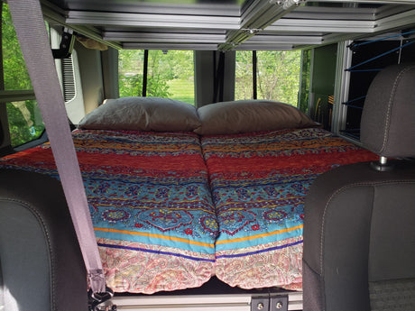 Comfortable sleeping area in an RV rental camper van. Features a colorful bed, pillows, and modular storage system.
