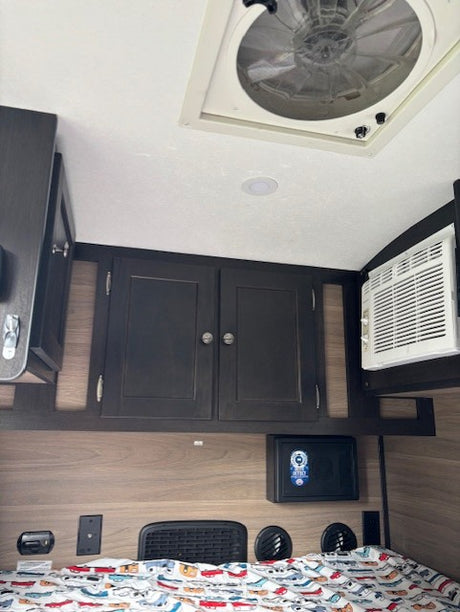 This RV rental shows a cozy bedroom with car-themed bedding, overhead storage, AC, ceiling fan, and a small wall safe.