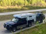 Dark blue F-series pickup with an RV rental truck camper towing a UTV, set for outdoor adventure.