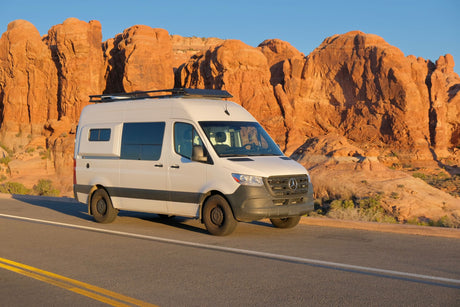 White Mercedes Sprinter RV rental on a road through red rock desert. Explore stunning landscapes by camper van.