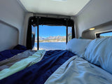 Cozy RV rental bed with a stunning lake and mountain view, perfect for a serene road trip adventure.