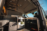 Inside a modern RV rental camper van: compact kitchen, Lagun table, fridge, and overhead storage.