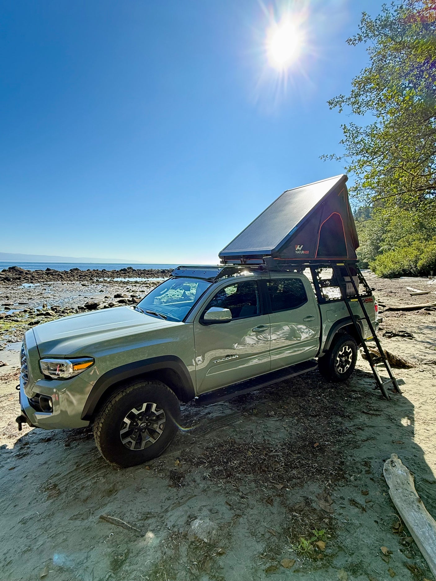 A light green Toyota Tacoma with a rooftop tent on a sunny beach, offering RV rental-like freedom for outdoor escapes.