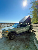 A light green Toyota Tacoma with a rooftop tent on a sunny beach, offering RV rental-like freedom for outdoor escapes.