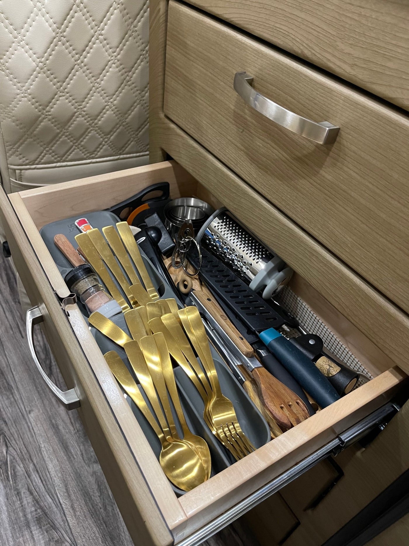 RV rental kitchen drawer open, revealing golden flatware, grater, and cooking tools, organized for compact living. — photo 10