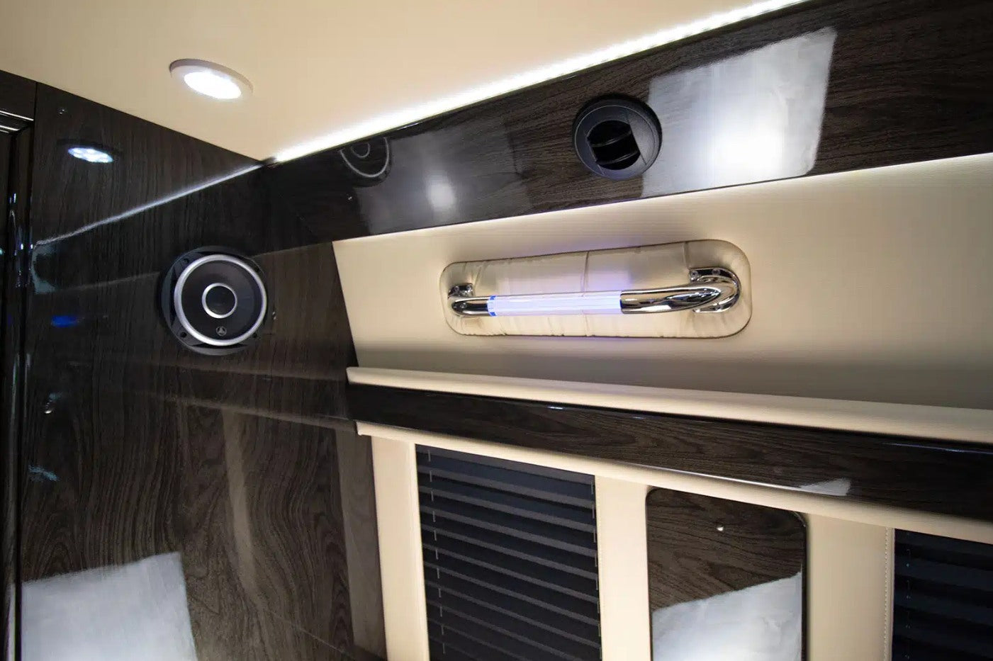 Luxury RV rental interior showing glossy dark wood, ceiling lights, a speaker, air vent, and an illuminated grab handle.