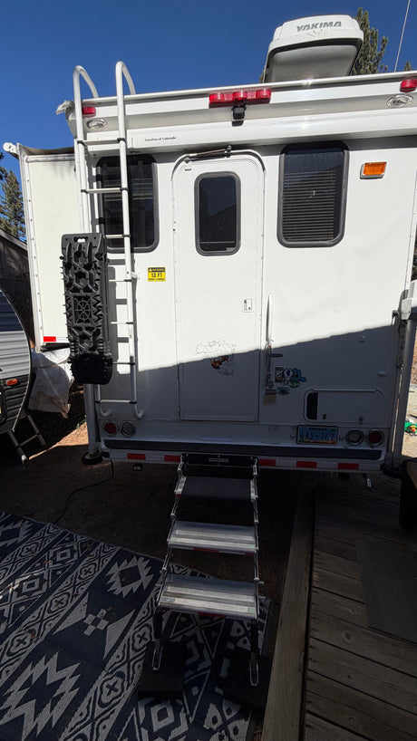 White rv rental camper's rear exterior shows a ladder, entry steps, a Yakima cargo box, and a Nevada license plate.