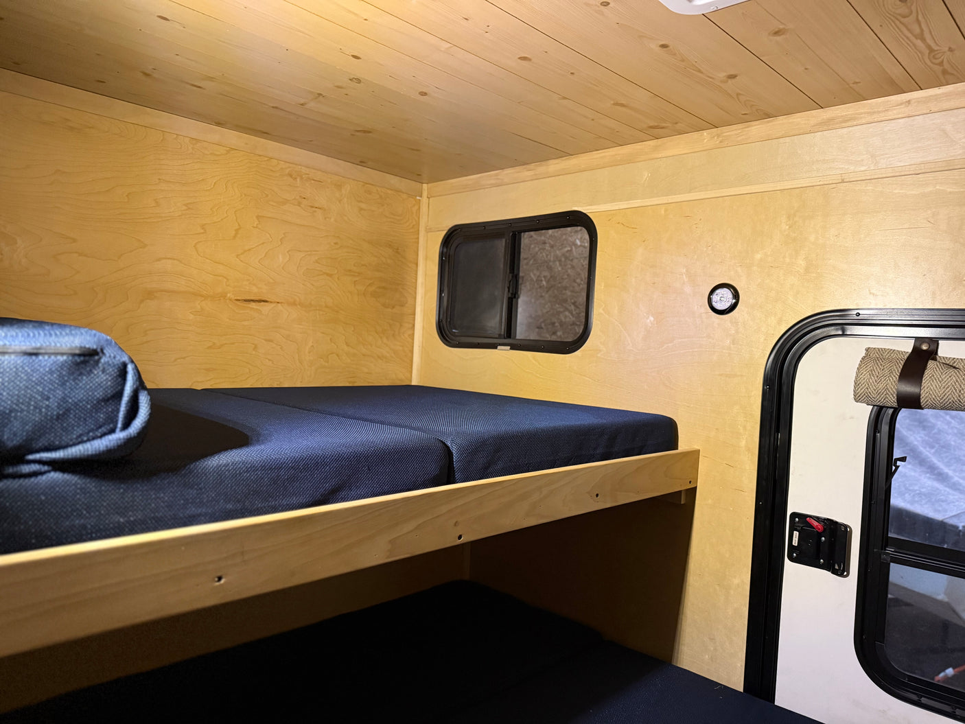 Cozy RV rental interior: wood-paneled walls/ceiling, dark blue bunk beds, window, and a door visible inside.