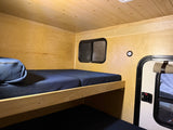 Cozy RV rental interior: wood-paneled walls/ceiling, dark blue bunk beds, window, and a door visible inside.