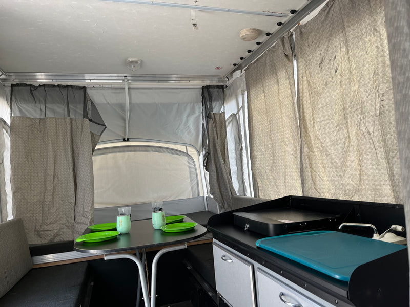 Cozy pop-up camper RV rental interior, featuring a dining area with a table and a compact kitchenette. — photo 13