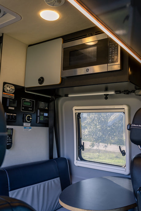 RV rental interior showcasing a microwave, control panel, and dining space. Efficient design for travel adventures.