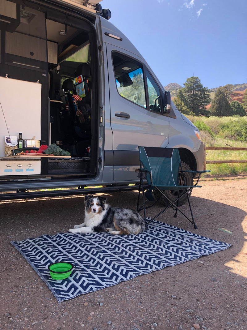 Relaxing RV rental setup: a grey camper van, dog on a mat, camping chair, and outdoor kitchen at a scenic campsite. — photo 17