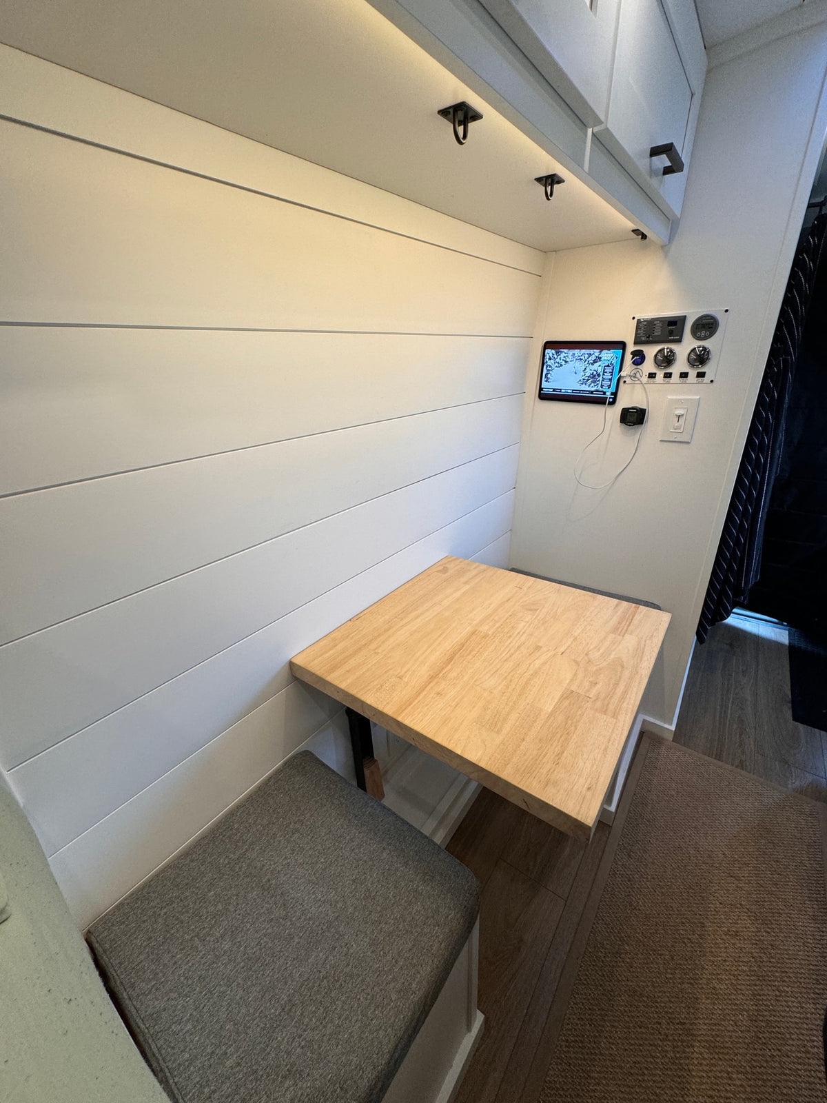 Cozy dining and control panel area in an RV rental, featuring a wooden table, gray bench, and white shiplap walls. — photo 7