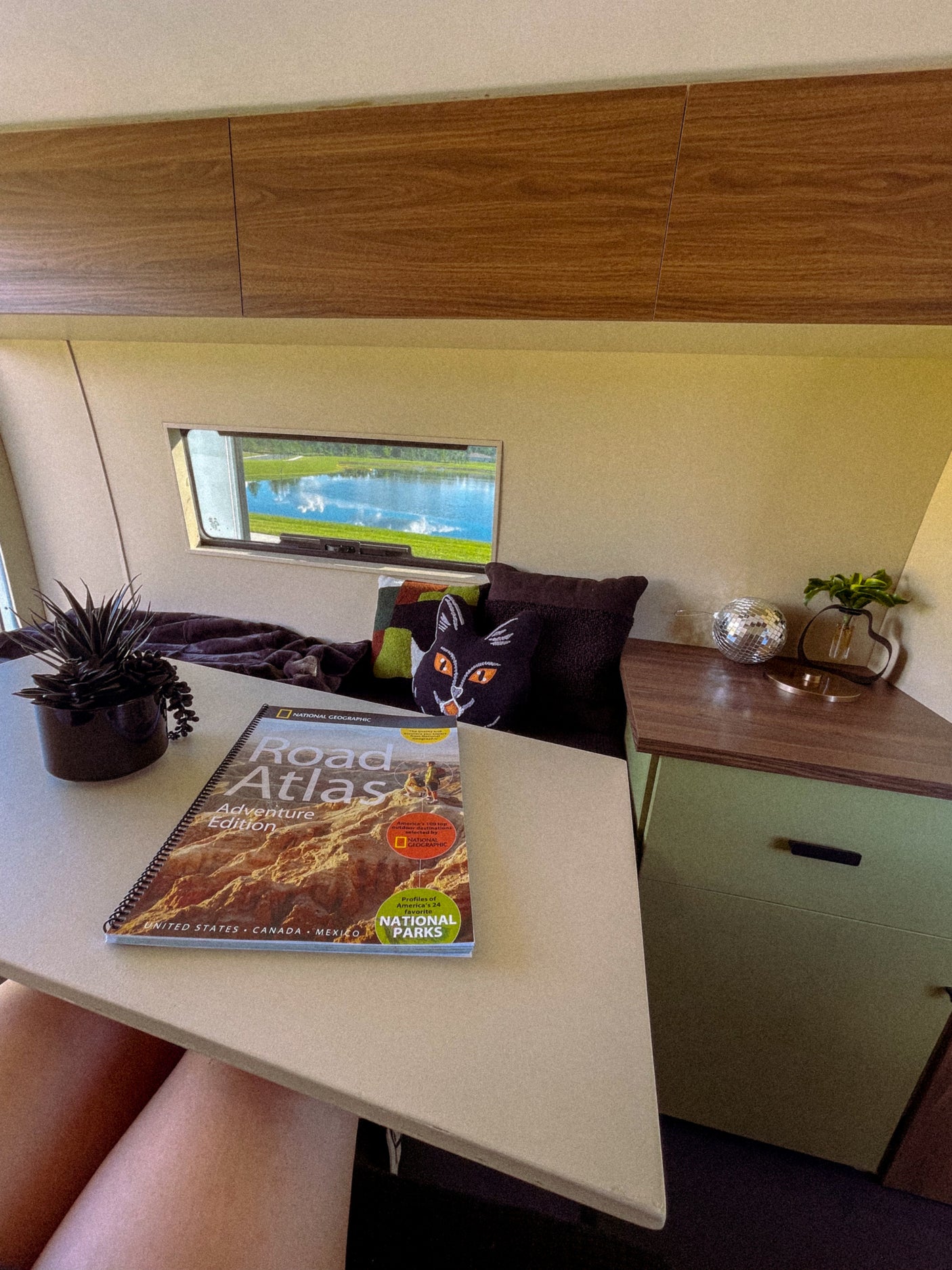 Cozy rv rental interior featuring a National Geographic Road Atlas. Planning adventures with a lake view outside and comfy decor.