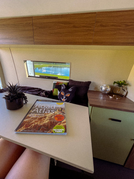 Cozy rv rental interior featuring a National Geographic Road Atlas. Planning adventures with a lake view outside and comfy decor.
