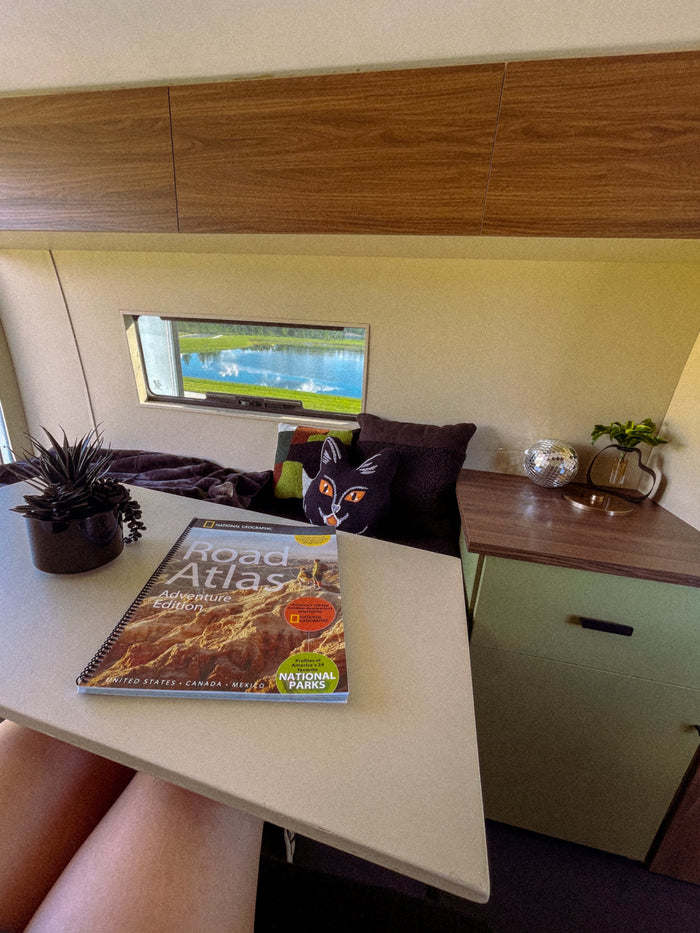 Cozy rv rental interior featuring a National Geographic Road Atlas. Planning adventures with a lake view outside and comfy decor.