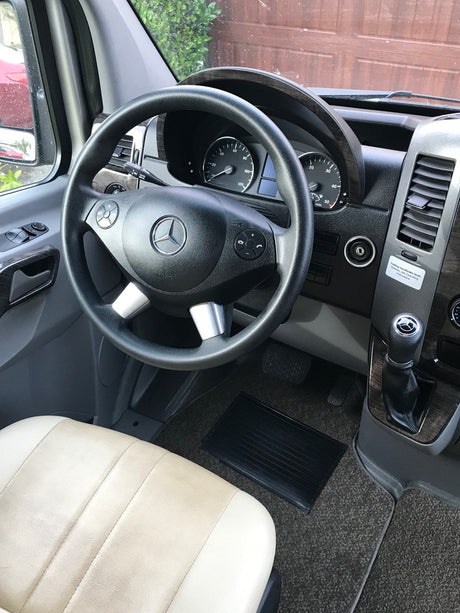 Inside a Mercedes-Benz RV rental, showing the driver's cabin with the steering wheel, dashboard, and light-colored seat.