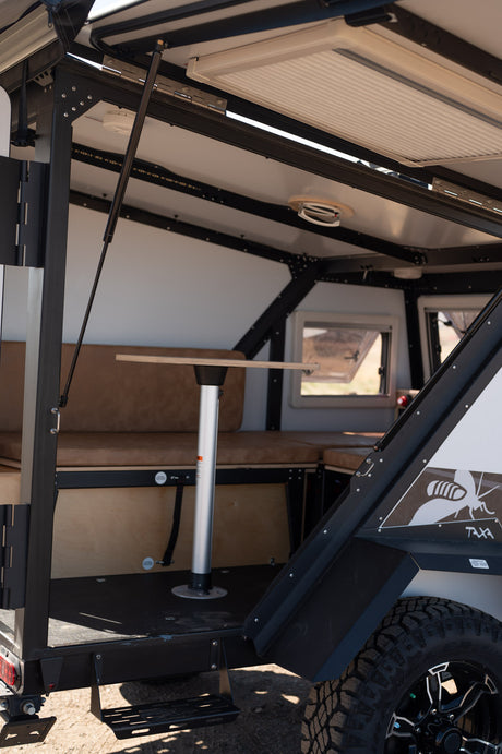 Explore this RV rental camper's interior: a cozy dinette with tan cushions, central table, & bright windows for adventure.