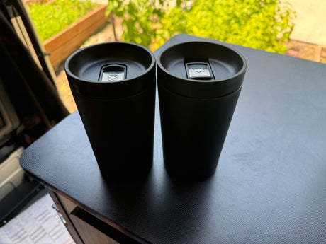 Two black travel mugs on a dark, textured table inside an RV rental, ready for any road trip.