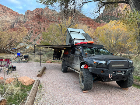 Overlanding truck with rooftop tent, solar, & awning at a scenic red rock campsite. A rugged adventure RV rental!