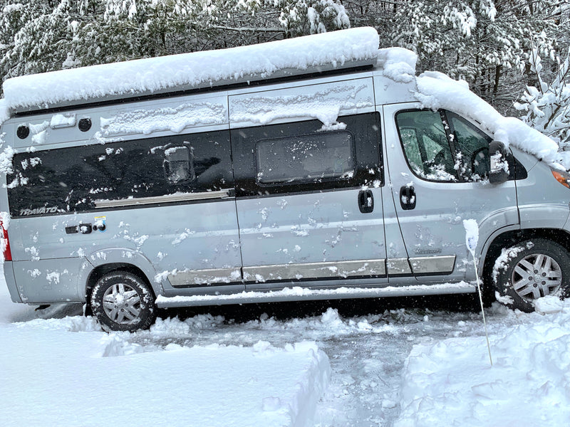 This silver Winnebago Travato rv rental is buried in fresh snow during a winter storm, with snowy trees in the background. — photo 13