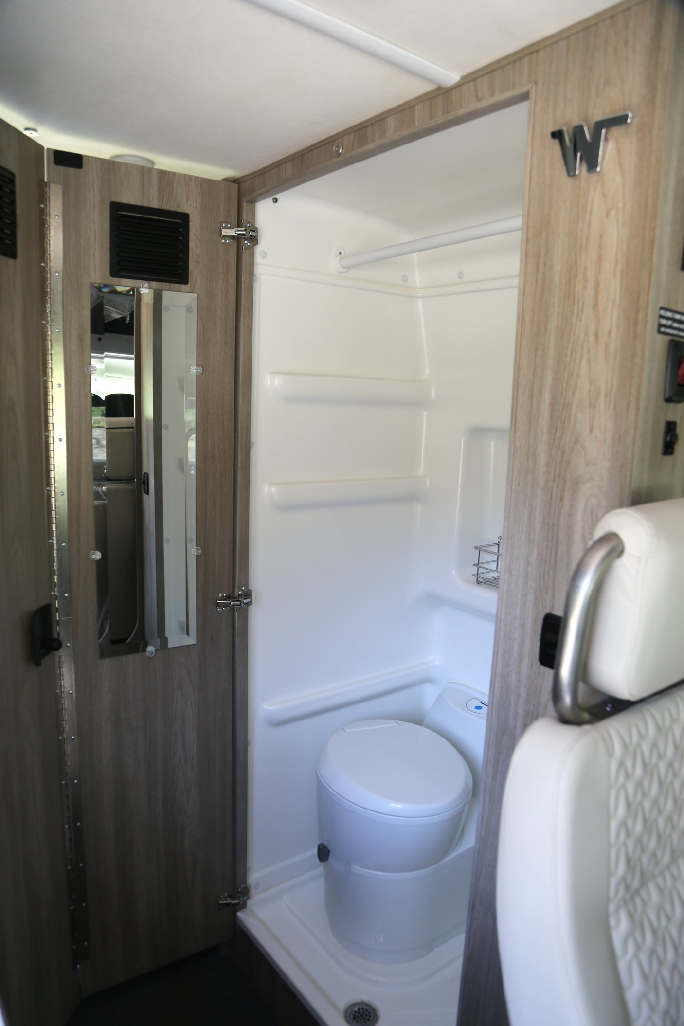 This RV rental's compact wet bath features a white toilet and shower area, designed for efficient camper interior use.