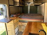 This rv rental shows a functional camper van interior with a striped bed, wood counters, and compact toilet.