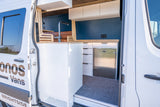 An RV rental: Inside a white camper van, a modern kitchen with a sink, refrigerator, and cabinet storage is visible.