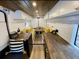 Stylish RV rental interior with wood ceiling, white walls, and yellow dinette seating. Perfect for van life adventures.