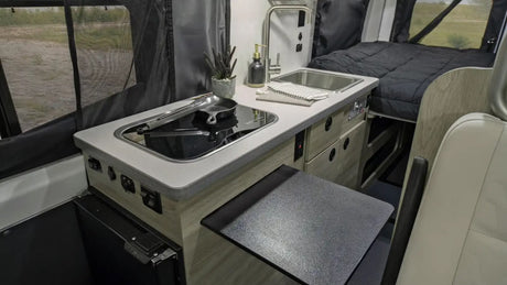 Explore this RV rental's interior: a compact kitchen with cooktop & sink, and a comfy bed. Perfect for mobile adventures.