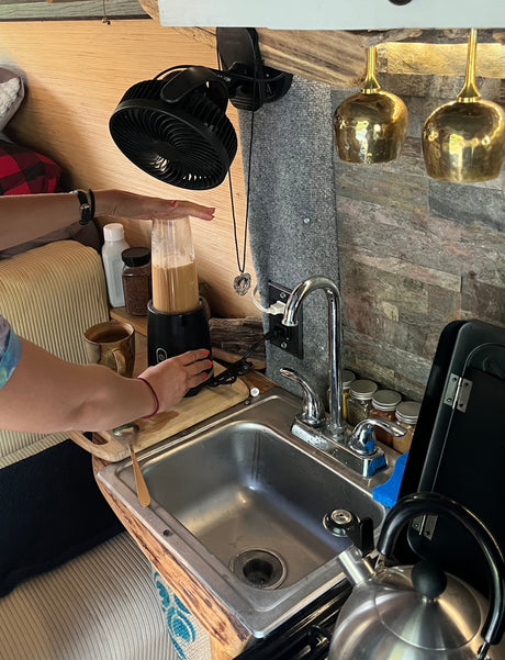 Hands blend a drink in a compact RV rental kitchen, featuring a sink, small appliances, and cozy details for travel.
