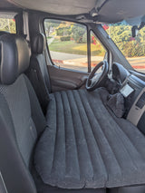 Interior of an RV rental showing a full-length inflatable mattress set up as a bed across the front seats of the van.