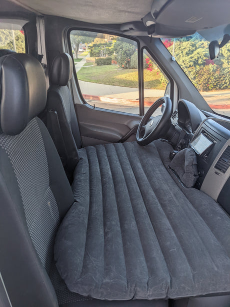 Interior of an RV rental showing a full-length inflatable mattress set up as a bed across the front seats of the van.