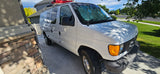 White Ford van, perfect for rv rental, parked in a sunny driveway next to a stone-front house.
