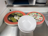 RV rental kitchen prep: Colorful camping plates & white bowls stacked on a metallic counter, ready for adventure.