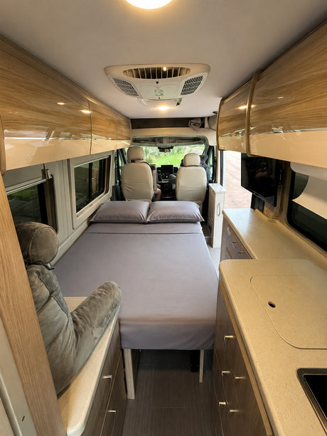 View inside an rv rental camper van: comfortable bed, sleek overhead cabinets, kitchen counter, and front seats.