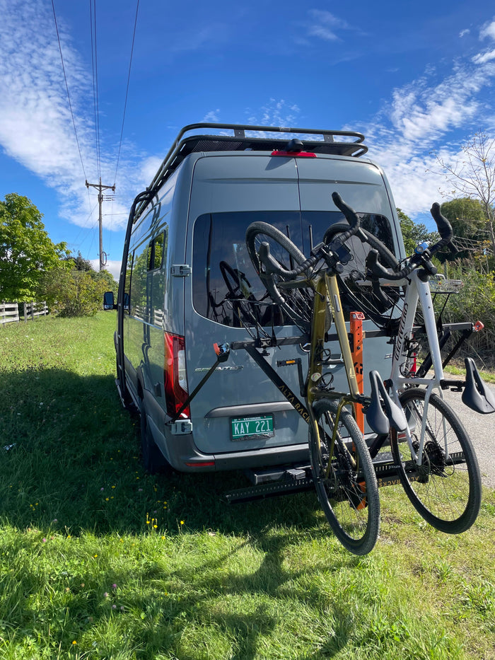 Grey RV rental van with two bicycles on its rear rack, parked on grass. Perfect for outdoor cycling adventures!