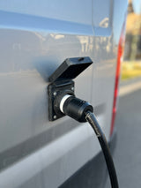 This RV rental is connected to shore power. A black electrical cord is plugged into the gray van's outdoor inlet.