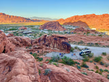 Elevated view of a stunning desert campground with red rock formations, featuring an RV rental and other vehicles.