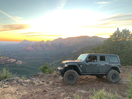 Gray Jeep on rocky overlook, vivid sunset over red rock mountains. Experience raw adventure, different from an rv rental trip.