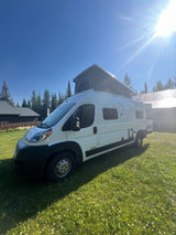 White pop-top camper van bathed in sun on a grassy field, ready for your next RV rental adventure.
