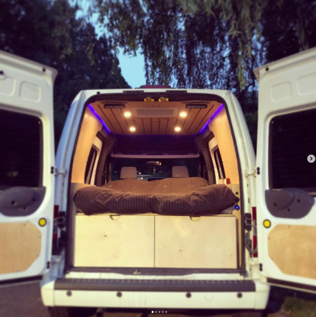 Inside this custom RV rental camper van: full bed, built-in storage, and ambient purple & warm lighting. Ready for adventure!