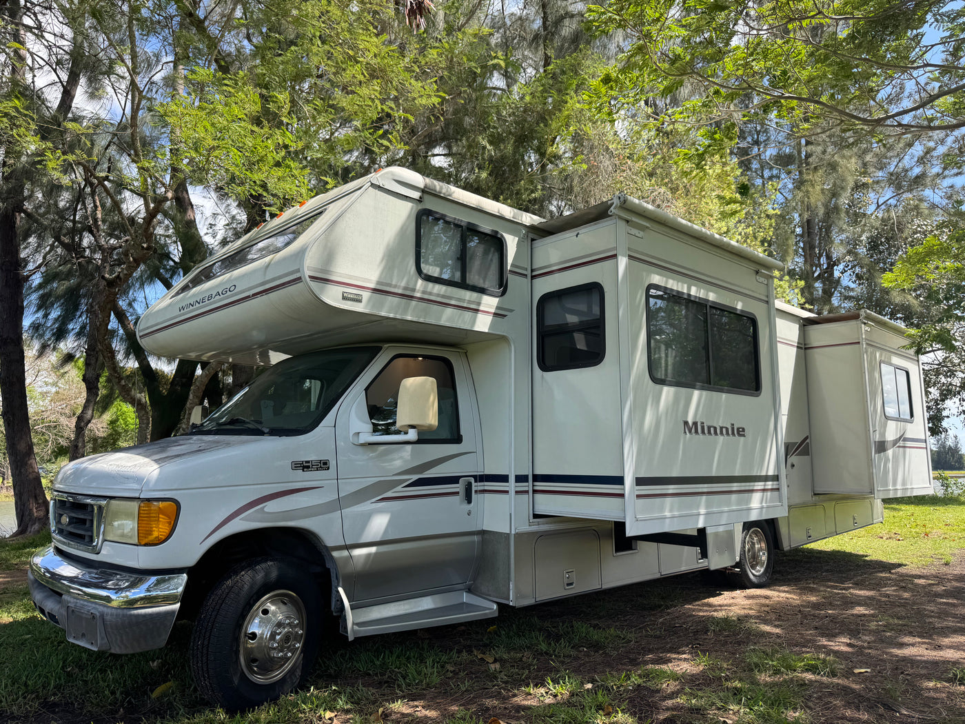 White Winnebago Minnie Class C RV rental with slide-out extended, parked among trees. A spacious motorhome ready for adventure. — photo 2