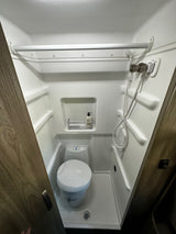 Inside a compact RV rental wet bath, featuring a toilet, shower, and overhead hanging bar. All-in-one convenience.