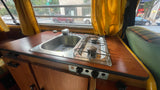 RV rental interior featuring a compact kitchen with a built-in sink, two-burner stove, and city street view.