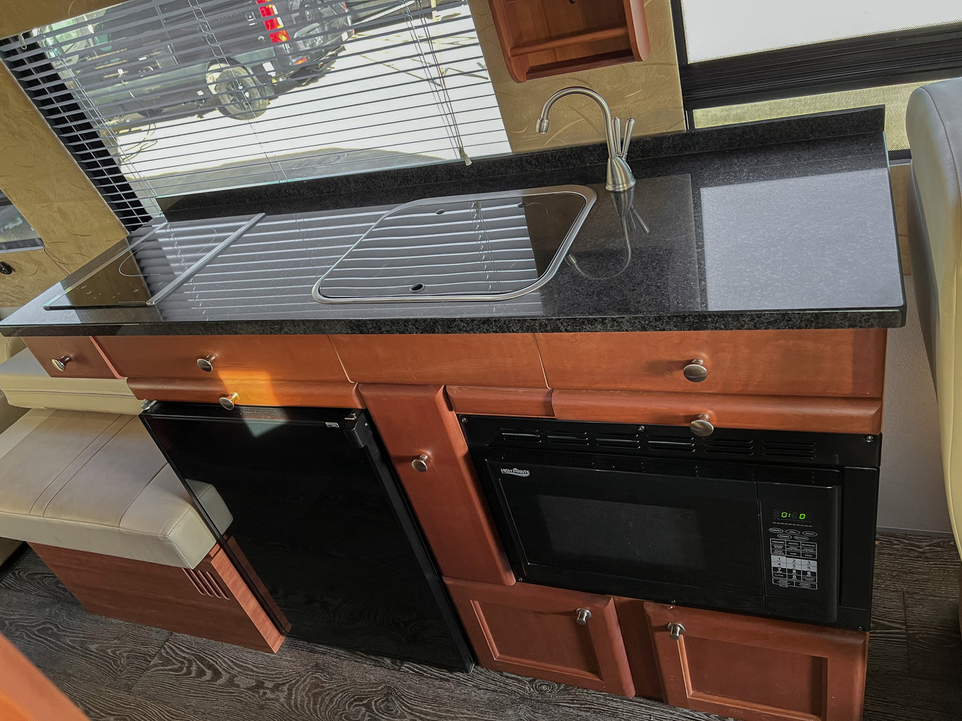 RV rental kitchen featuring a sleek black granite counter, stovetop, sink, microwave, fridge, and window with blinds. — photo 12