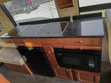 RV rental kitchen featuring a sleek black granite counter, stovetop, sink, microwave, fridge, and window with blinds.
