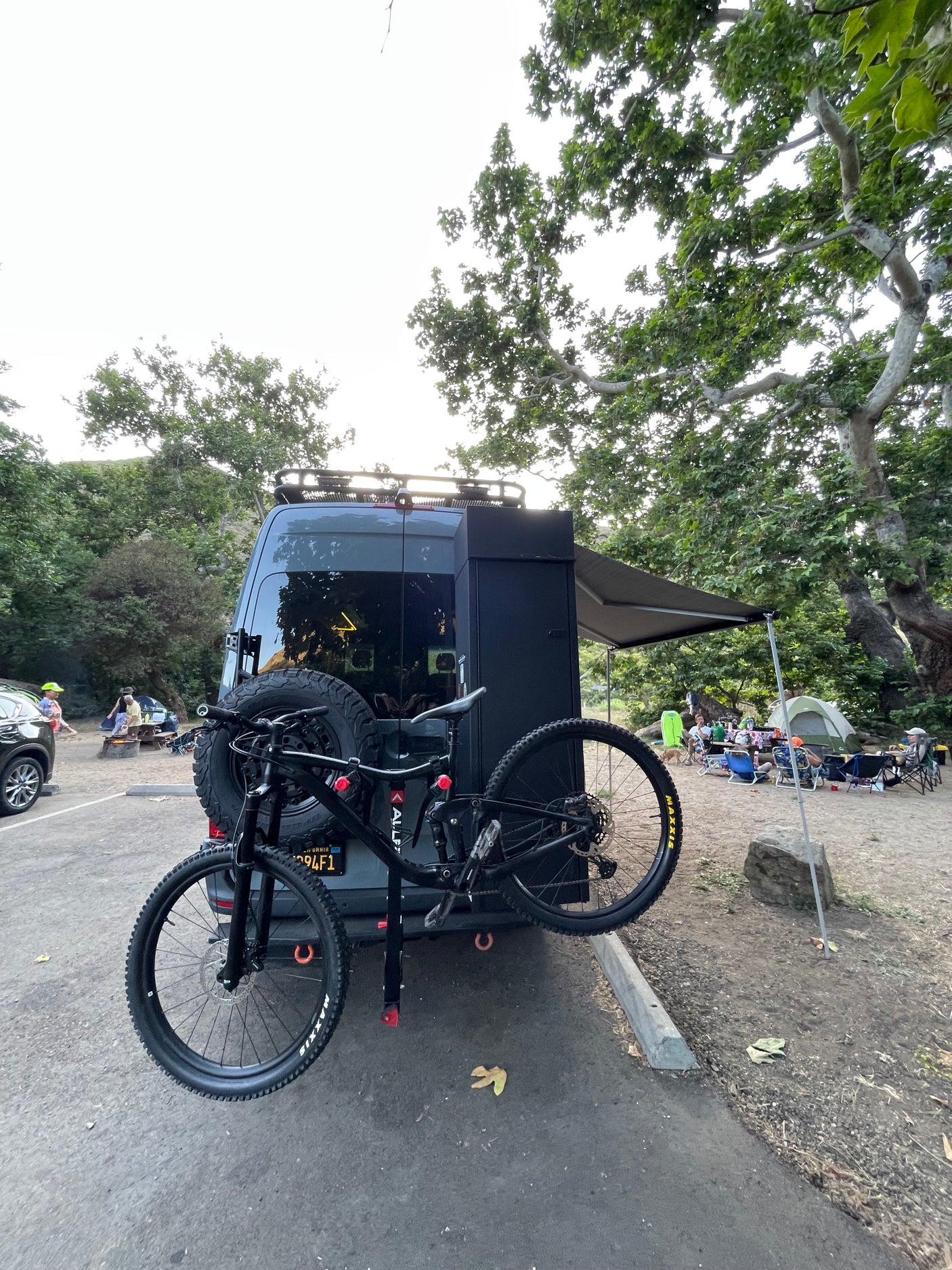 Adventure-ready RV rental with bike rack at a lively campsite, perfect for outdoor enthusiasts.