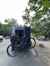 Adventure-ready RV rental with bike rack at a lively campsite, perfect for outdoor enthusiasts.