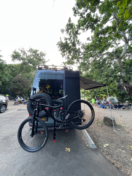 Adventure-ready RV rental with bike rack at a lively campsite, perfect for outdoor enthusiasts.